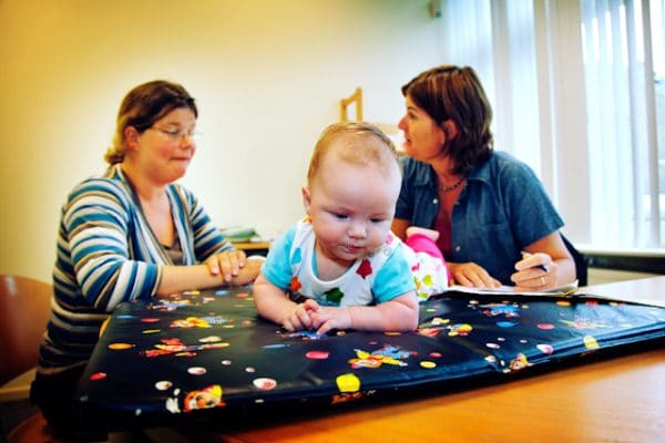 Een ouder praat met een CJG-professional terwijl een baby op zijn buik op een mat ligt.