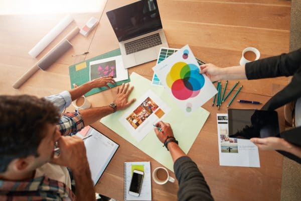 Grafisch ontwerpers die een design bespreken aan een tafel met daarop onder andere een laptop, potloden en vellen papier