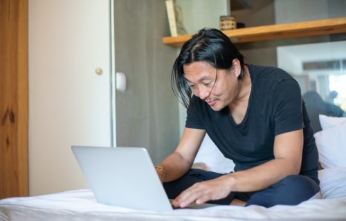 Een man zit op een bed en bedient een laptop
