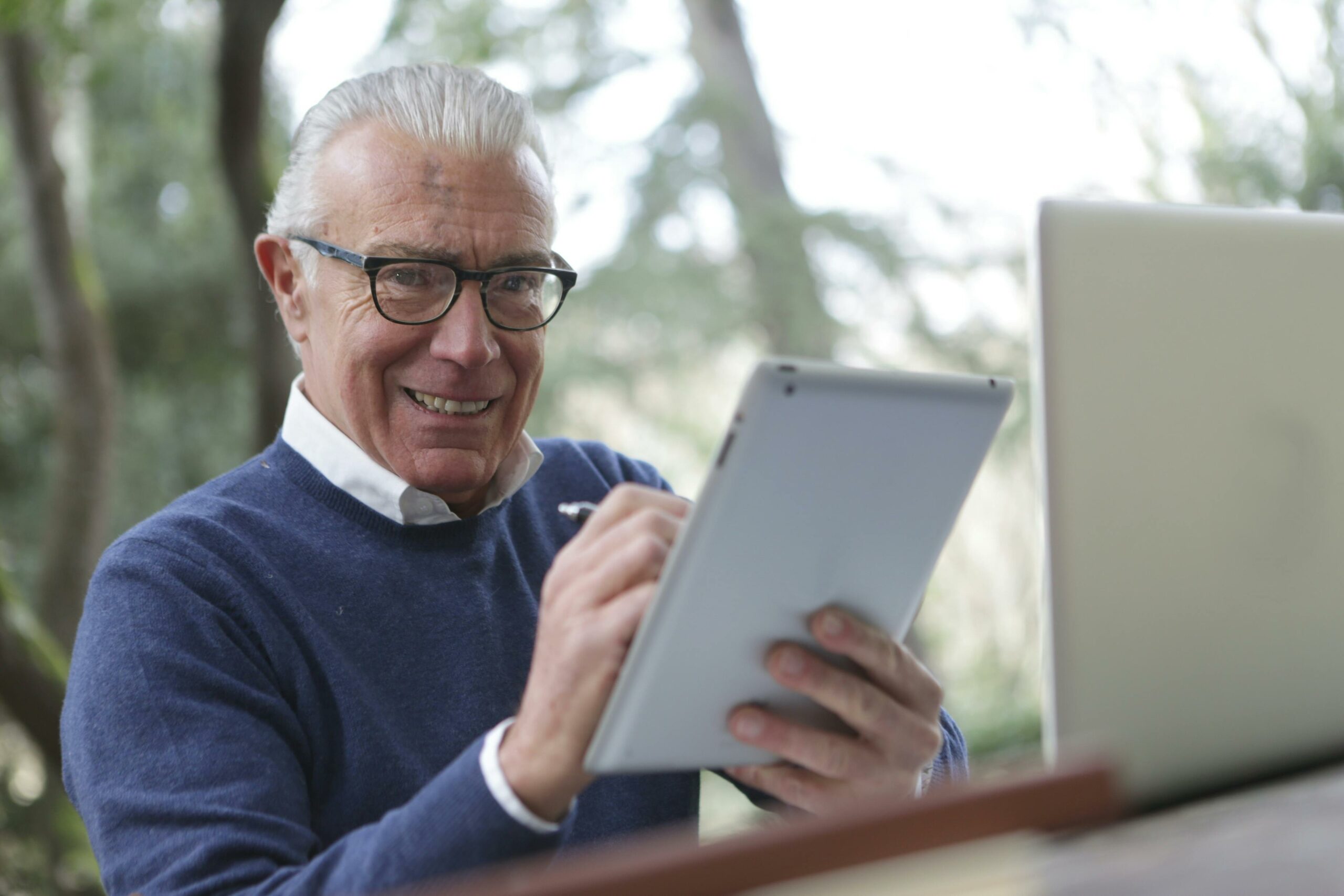 Man met bril en grijs haar kijkt enthousiast naar zijn tablet